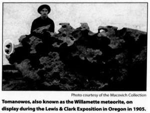 Photograph of a man standing next to the meteorite, which is almost as tall as he is. Caption reads: "Tomanowos, also known as the Willamette meteorite, on display during the Lewis and Clark Exposition in Oregon in 1905." Photo courtesy of the Macovich Collection.